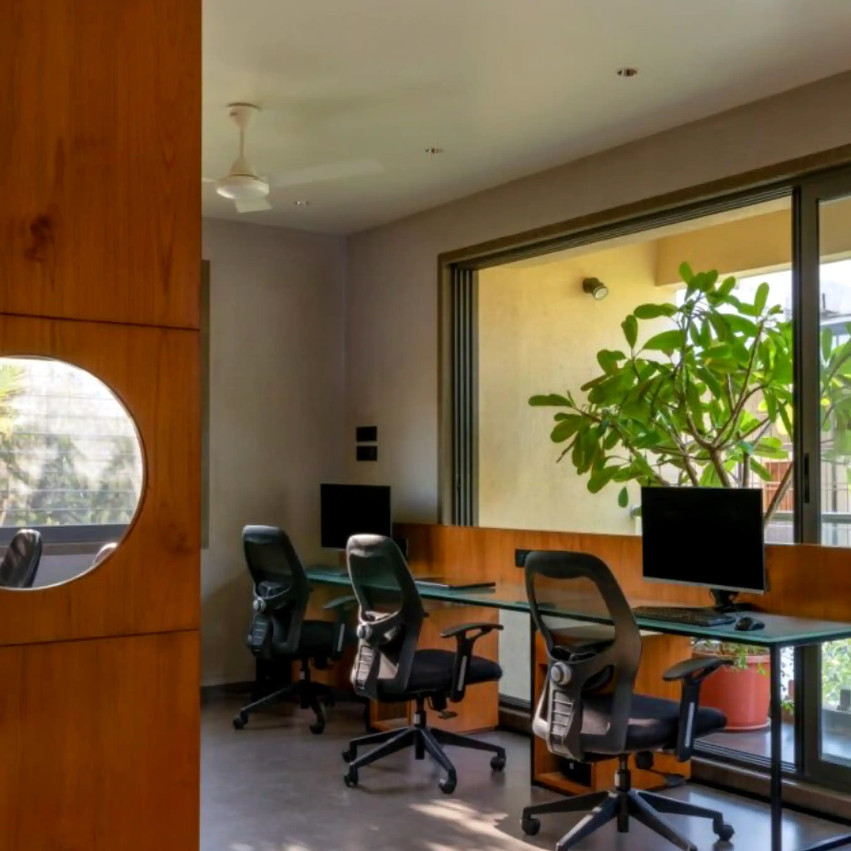 Glass-topped workstations with wood partitions and ergonomic chairs by the window